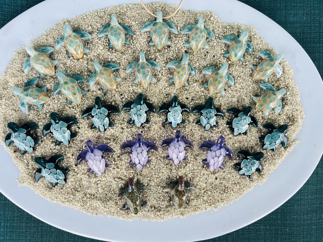 Handcrafted glass sea turtle figurines arranged on sand — Maggies Gems Glass Art